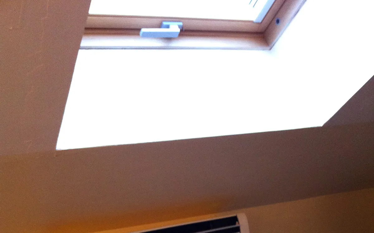 Console de climatisation murale posee sous un velux dans une chambre amenagee en combles